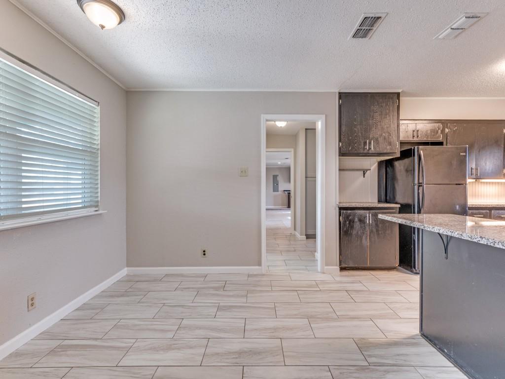 7325 Reed Road Azle, TX 76020 - Photo 17 of 38 Kitchen with dark brown cabinetry, a textured ceiling, light stone counters, freestanding refrigerator, and a kitchen breakfast bar