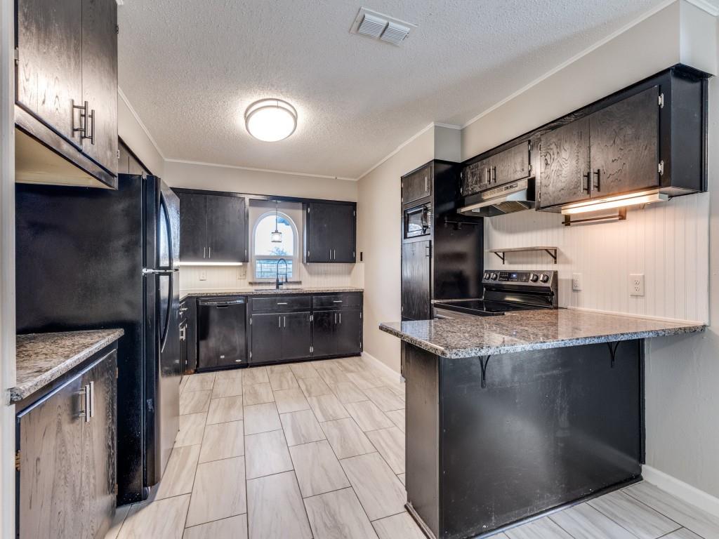 7325 Reed Road Azle, TX 76020 - Photo 18 of 38 Kitchen with a textured ceiling, a kitchen bar, dark stone counters, black appliances, and dark cabinetry