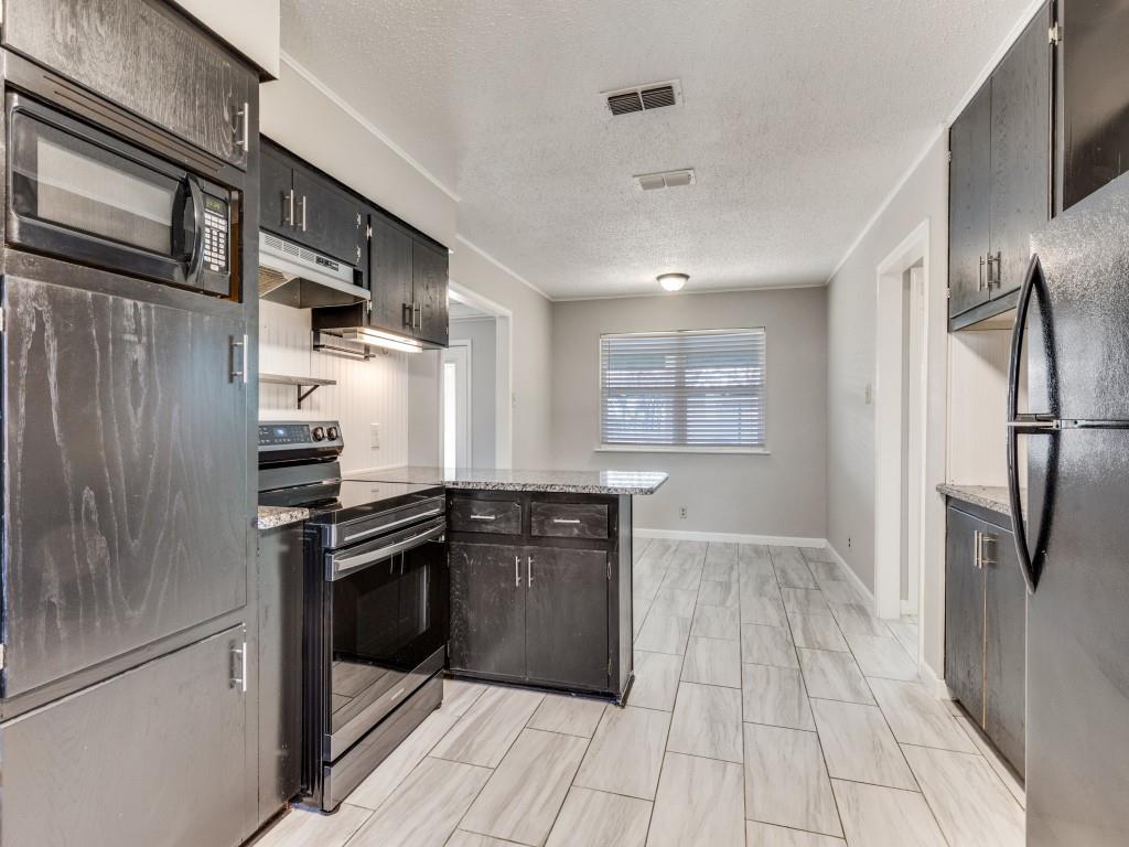 7325 Reed Road Azle, TX 76020 - Photo 20 of 38 Kitchen with a peninsula, black appliances, a textured ceiling, light stone countertops, and under cabinet range hood