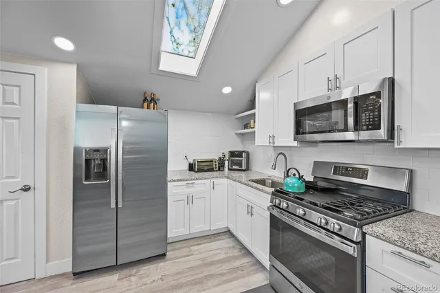 a kitchen with stainless steel appliances granite countertop a stove top oven a sink dishwasher a refrigerator and white cabinets with wooden floor