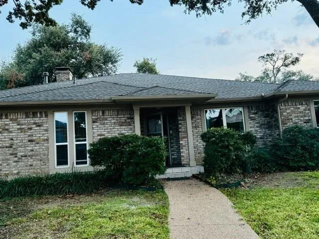 a view of a brick house with a large windows plants and large trees