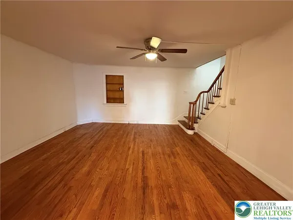 a view of empty room with wooden floor and fan