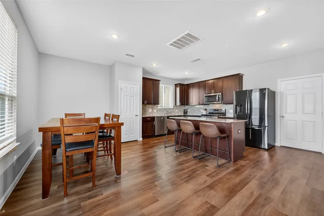 a kitchen with stainless steel appliances kitchen island granite countertop a table chairs sink and cabinets