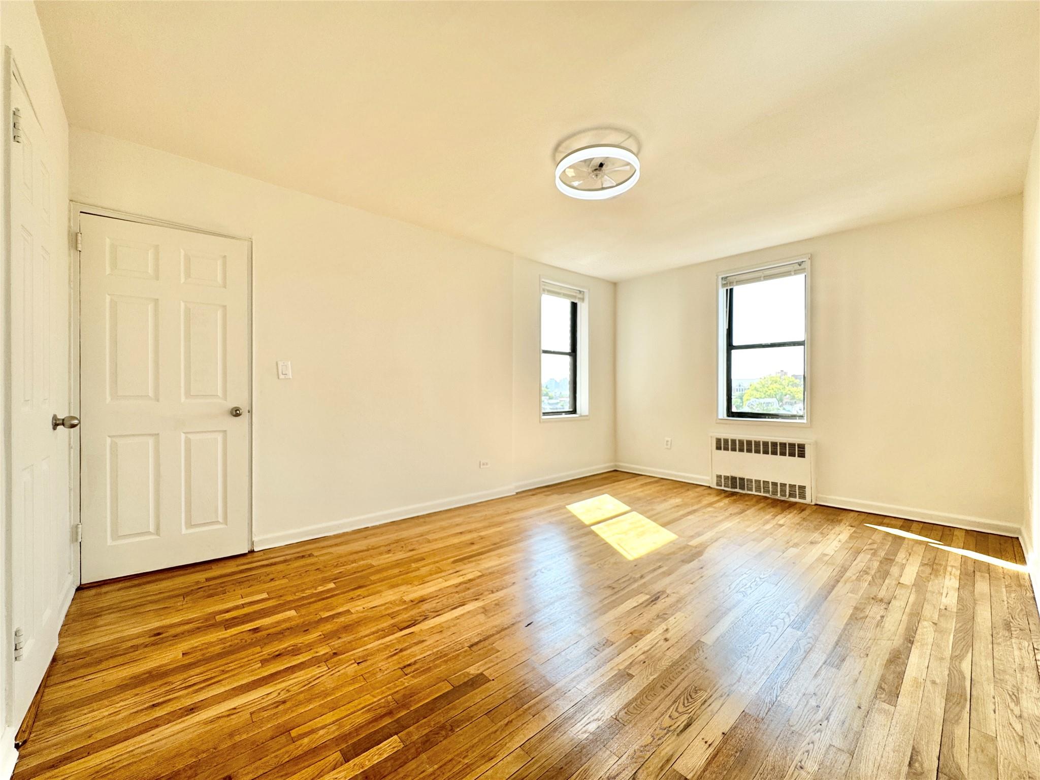 84-19 51st Avenue, Unit 5E Queens, NY 11373 - Photo 3 of 8 an empty room with wooden floor and windows