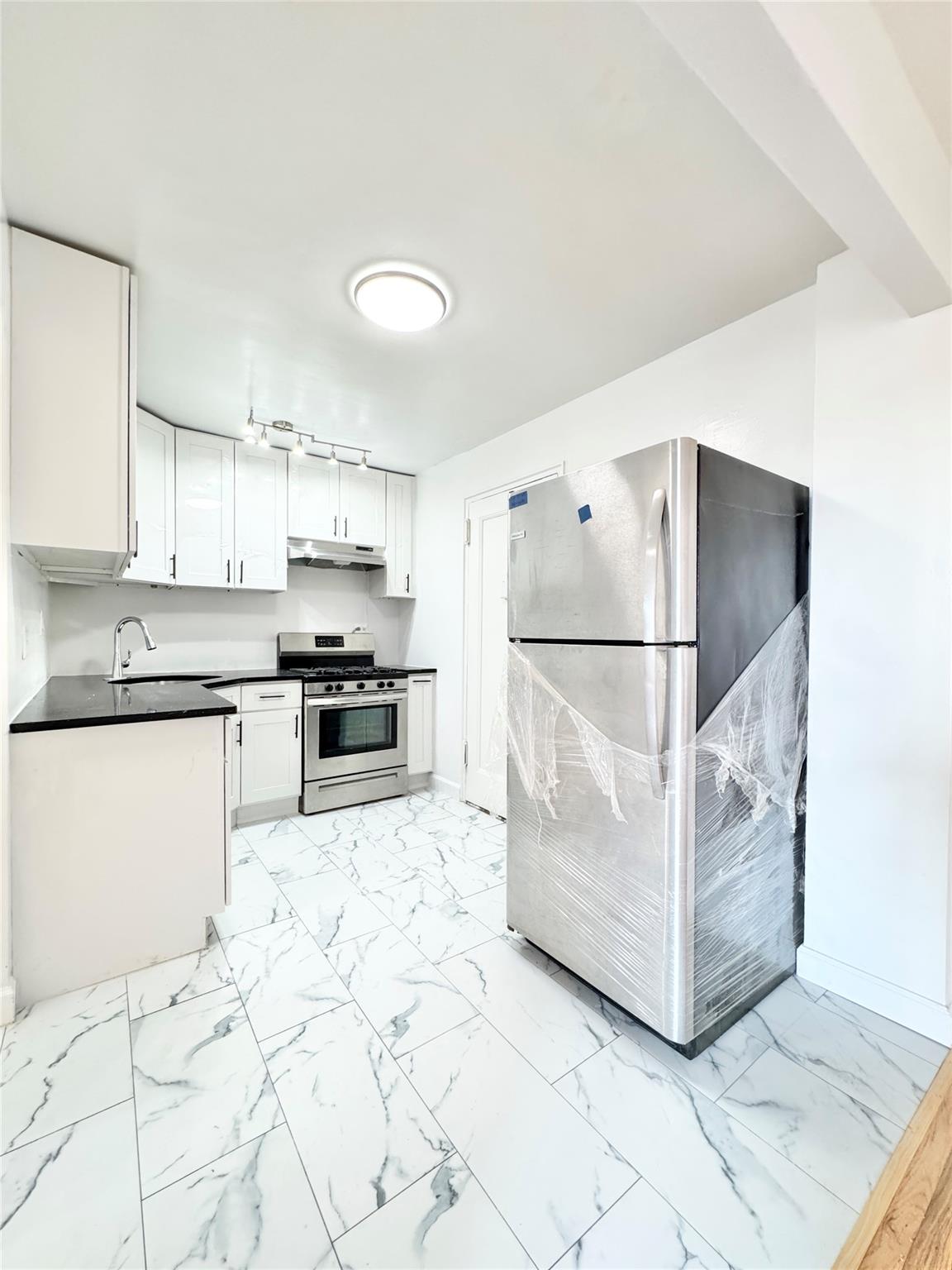 84-19 51st Avenue, Unit 5E Queens, NY 11373 - Photo 6 of 8 a kitchen with granite countertop a refrigerator and a stove top oven