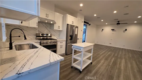 a kitchen with stainless steel appliances kitchen island granite countertop a stove a sink and a refrigerator with wooden floor