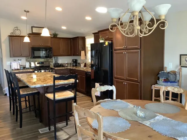 a kitchen with stainless steel appliances kitchen island granite countertop a refrigerator a stove a sink and a dining table with wooden floor