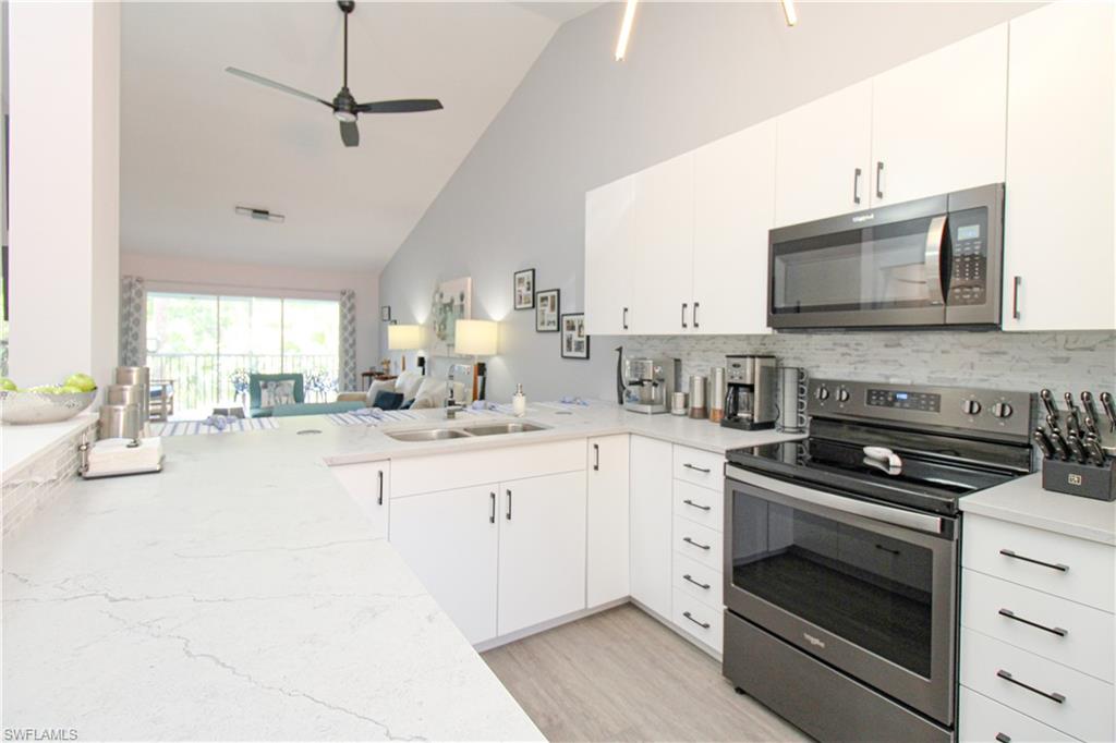 225 Robin Hood Circle, Unit 203 Naples, FL 34104 - Photo 13 of 50 Kitchen with ceiling fan, stainless steel appliances, light wood-type flooring, backsplash, and high vaulted ceiling