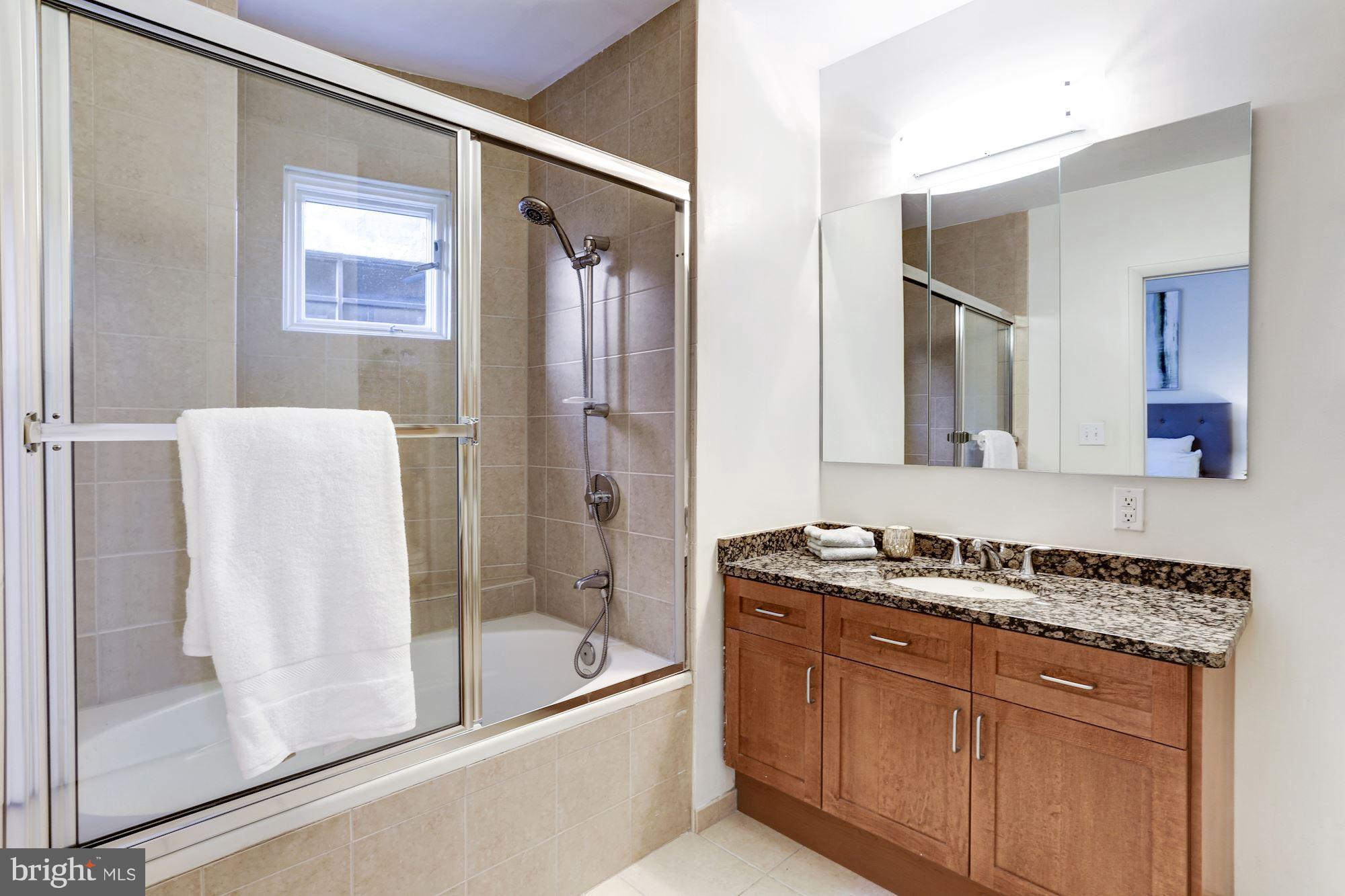 1700 Kalorama Road Northwest, Unit 312 Washington, DC 20009 - Photo 23 of 45 a bathroom with a granite countertop sink a mirror a bathtub and shower