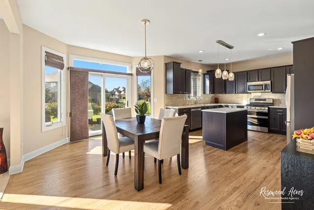 a open kitchen with stainless steel appliances granite countertop a stove a refrigerator a kitchen island a dining table and chairs with wooden floor