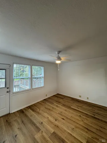an empty room with wooden floor fan and windows