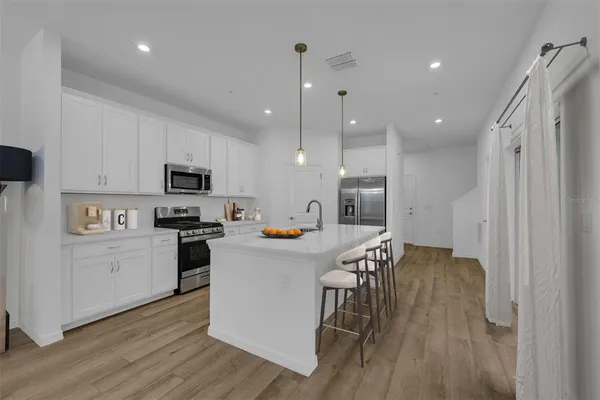 a kitchen with stainless steel appliances a refrigerator a stove top oven a sink dishwasher and white cabinets with wooden floor