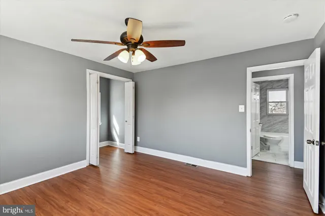 a view of an empty room with wooden floor and a ceiling fan