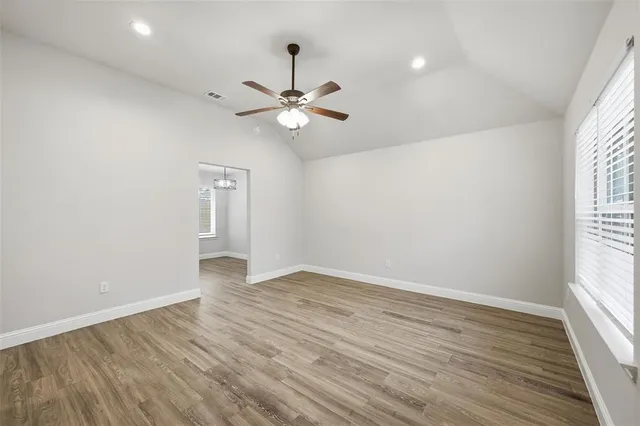 an empty room with wooden floor ceiling fan and windows