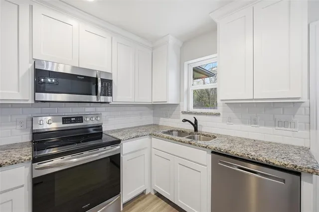 a kitchen with stainless steel appliances granite countertop a sink dishwasher a stove microwave and oven with white cabinets