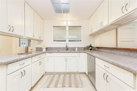 a kitchen with granite countertop white cabinets white appliances a sink and a window