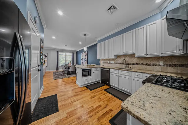 a kitchen with stainless steel appliances granite countertop a stove top oven a sink dishwasher and a refrigerator with wooden floor