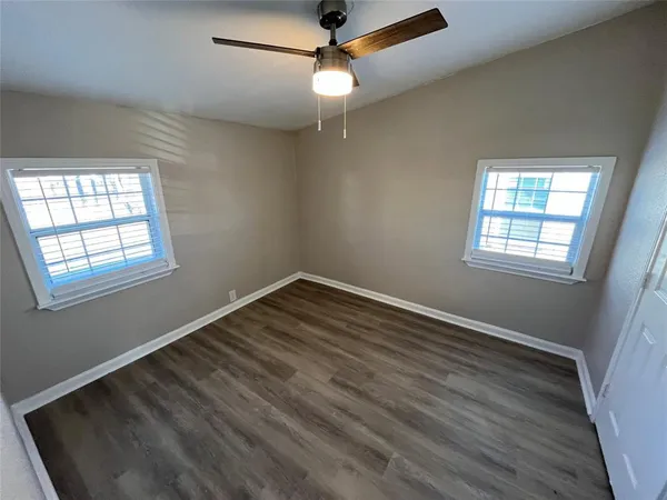 an empty room with wooden floor fan and windows