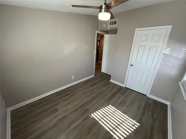 a view of an empty room with wooden floor and a ceiling fan