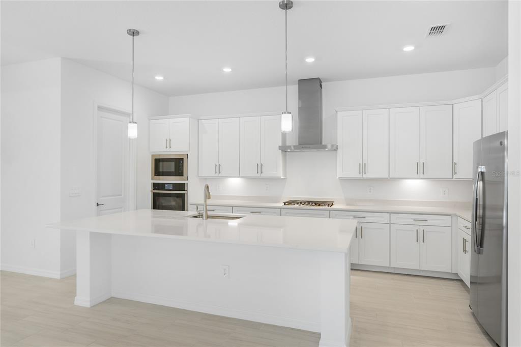 19156 Cherrystone Way Lakewood Ranch, FL 34211 - Photo 12 of 49 a large kitchen with stainless steel appliances kitchen island granite countertop a stove a sink a refrigerator and white cabinets with wooden floor