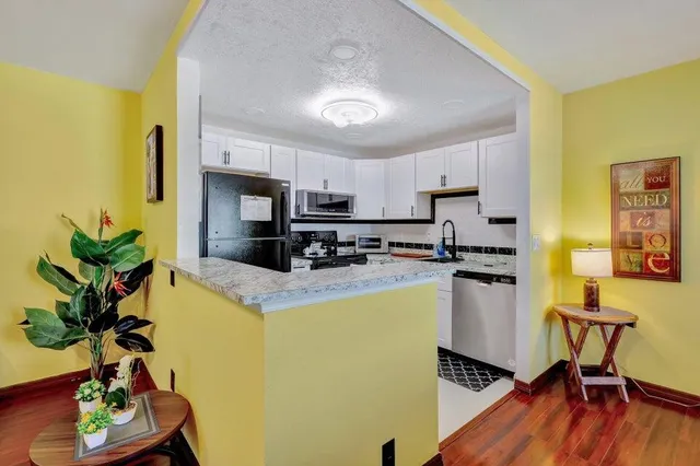 a kitchen with stainless steel appliances granite countertop a refrigerator a stove a sink dishwasher and a dining table with wooden floor