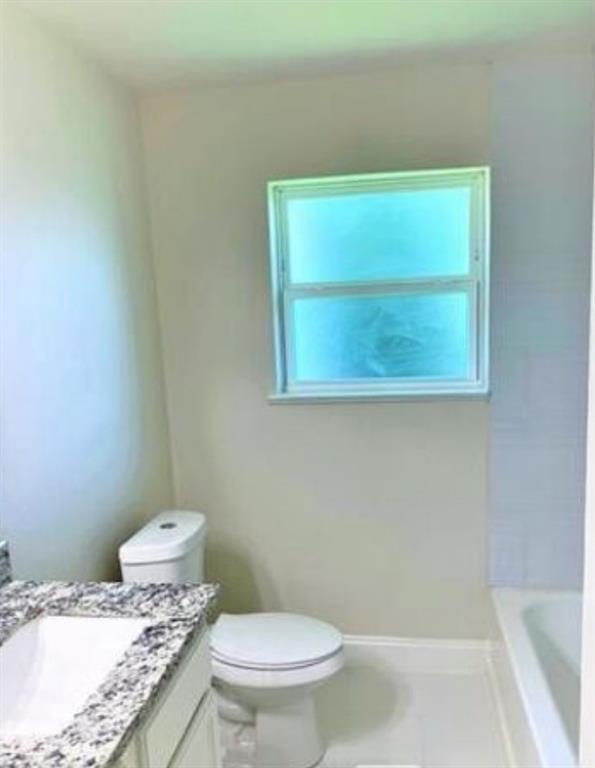 2536 Rutherford Street Irving, TX 75062 - Photo 12 of 19 Bathroom with a window, white tile flooring, a white toilet, and a vanity featuring a light-toned countertop
