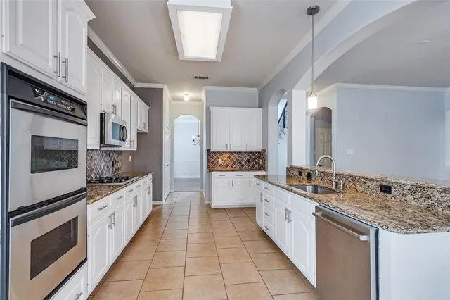 a large white kitchen with stainless steel appliances granite countertop a stove and a sink