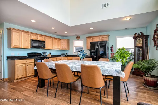 a kitchen with stainless steel appliances granite countertop a stove a refrigerator a kitchen island a dining table and chairs with wooden floor