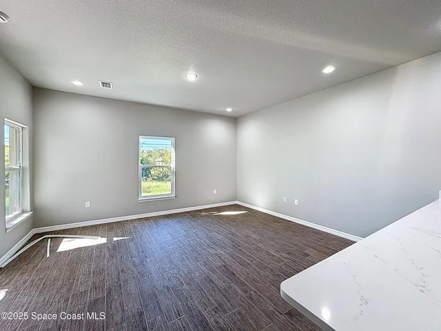 an empty room with wooden floor staircase and a kitchen