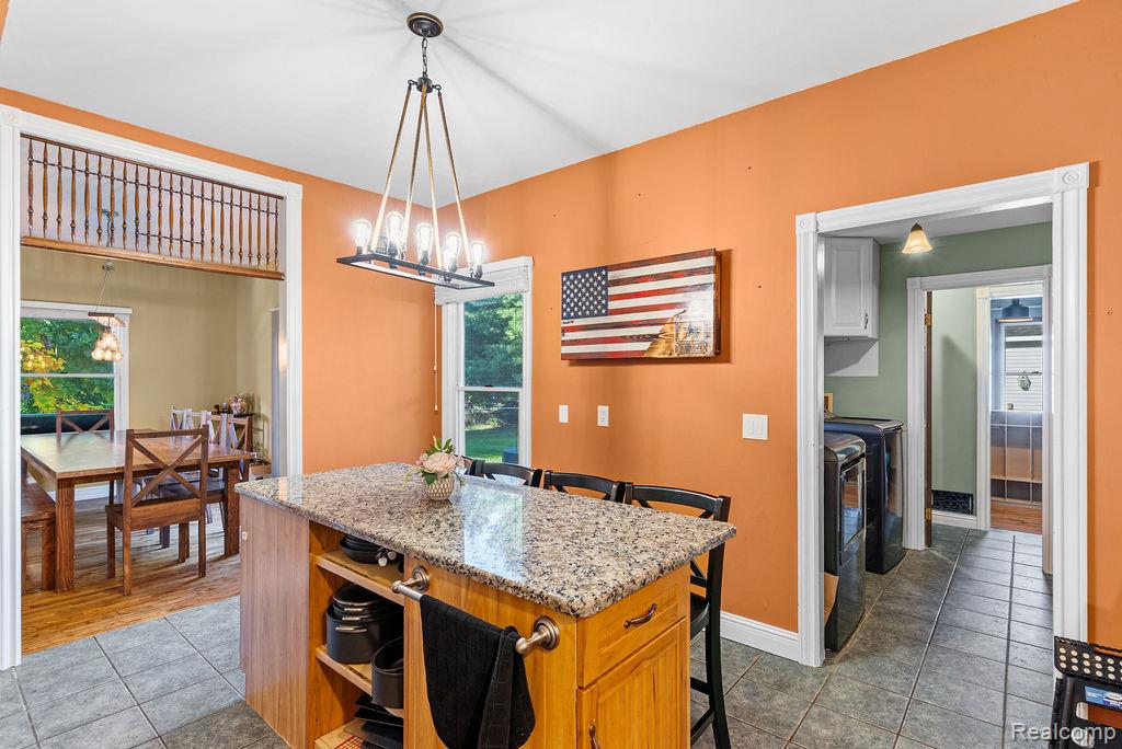 1476 County Farm Road Howell, MI 48843 - Photo 17 of 53 Kitchen featuring light tile patterned floors, light stone countertops, a kitchen breakfast bar, a kitchen island, and pendant lighting