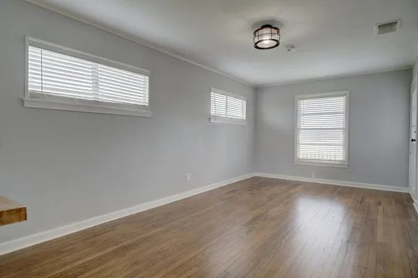 an empty room with wooden floor and windows with curtains