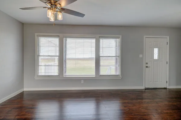 an empty room with wooden floor chandelier and windows