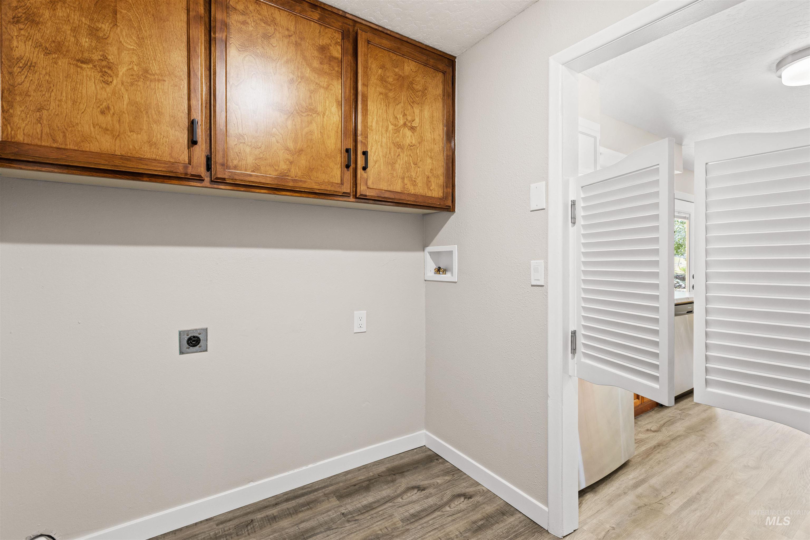 12184 Hill Road Payette, ID 83661 - Photo 19 of 35 Laundry area featuring wood-finish flooring, white baseboards, and overhead wood cabinetry with dark hardware