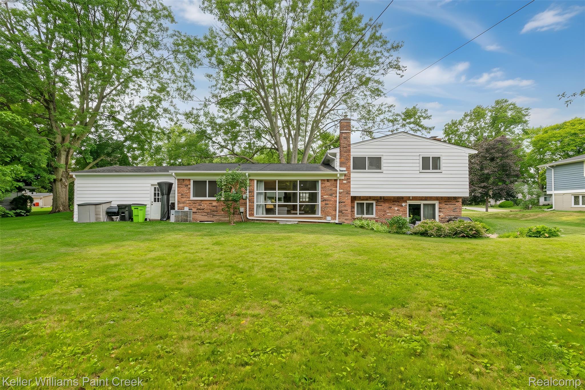 7093 Stonebrook Road West Bloomfield, MI 48322 - Photo 4 of 64 Expansive rear yard featuring a manicured lawn, mature trees, and a brick and siding exterior