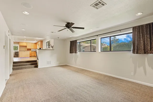 a view of an empty room with a window and kitchen view