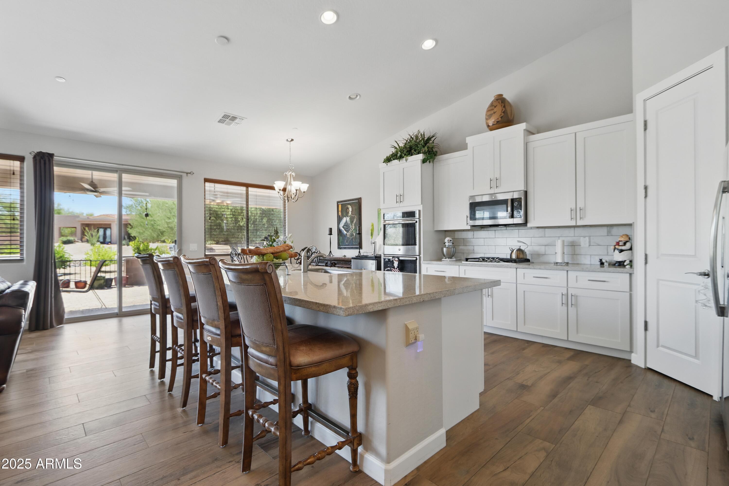 19023 East Buckskin Drive Rio Verde, AZ 85263 - Photo 5 of 31 a kitchen with kitchen island granite countertop a table chairs sink and white cabinets with wooden floor