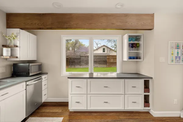 a kitchen with stainless steel appliances granite countertop a stove a sink dishwasher a refrigerator and white cabinets with wooden floor