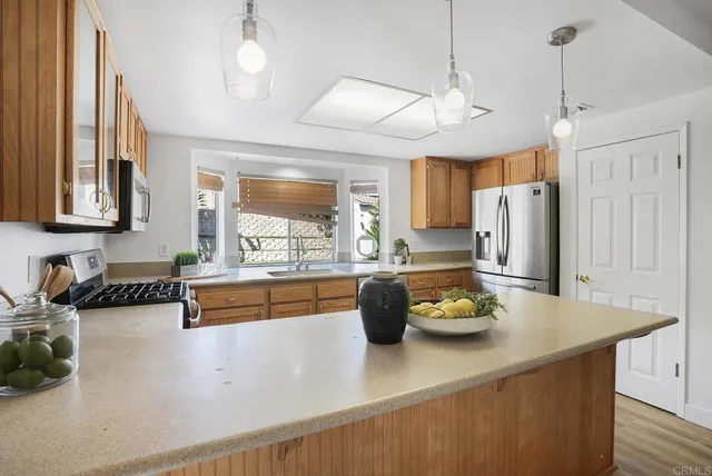 a kitchen with stainless steel appliances granite countertop a refrigerator a sink dishwasher a oven a dining table and chairs with wooden floor