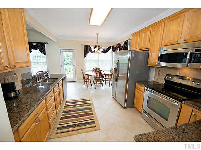 672 Seastone Street Raleigh, NC 27603 - Photo 7 of 23 Kitchen with granite countertops, stainless steel appliances including a smooth top range, backsplash, serving bar, pantry, crown molding and tile flooring.