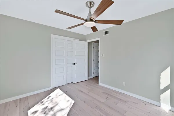 an empty room with wooden floor fan and windows