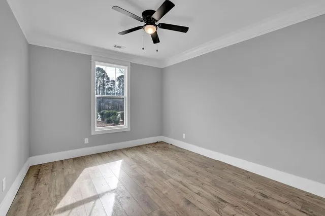 an empty room with wooden floor chandelier fan and windows
