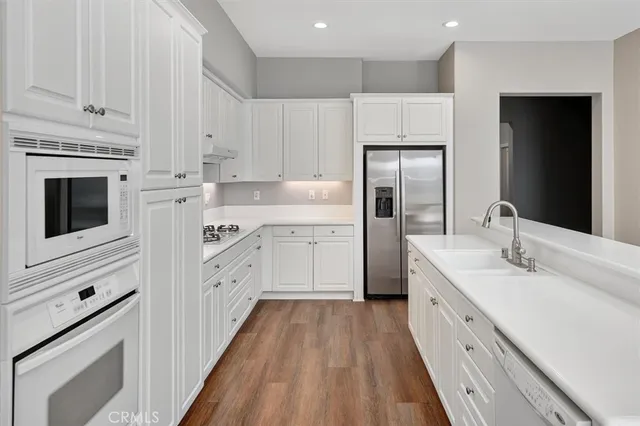a large white kitchen with a stove a sink dishwasher and a refrigerator with wooden floor