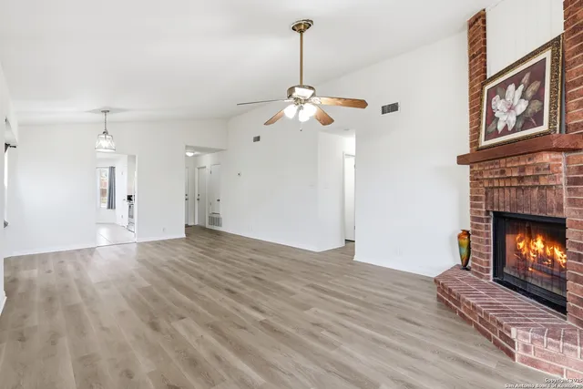 a view of an empty room with wooden floor fireplace and a window