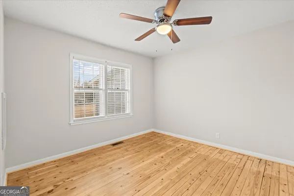 an empty room with wooden floor fan and windows