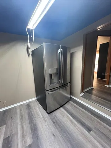 a view of a refrigerator in kitchen and an empty room with wooden floor