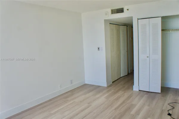 a view of an empty room with wooden floor and closet