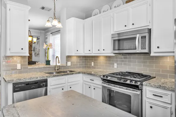 a kitchen with stainless steel appliances granite countertop a sink a stove and a white cabinets