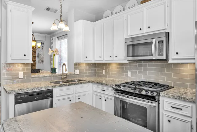 a kitchen with stainless steel appliances granite countertop a sink a stove and a white cabinets