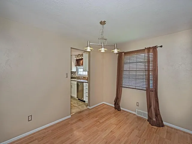 a view of empty room with wooden floor and kitchen