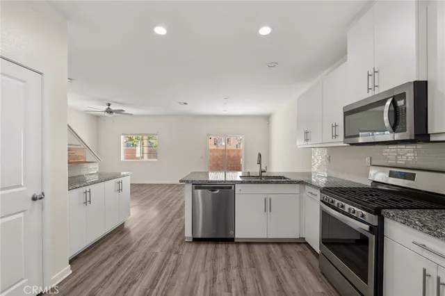 a kitchen with granite countertop a sink cabinets stainless steel appliances and wooden floor